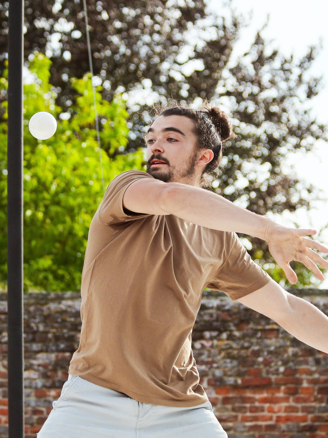 Un jongleur lance une balle blanche devant un mur de brique, le bras tendu